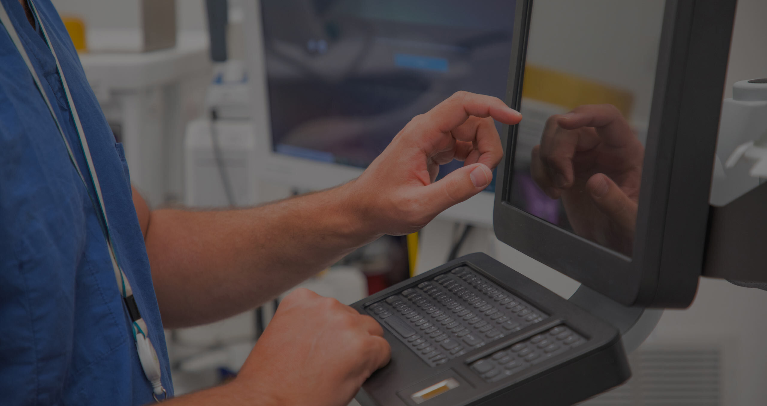 A person in scrubs interacts with a touchscreen device in a medical setting.